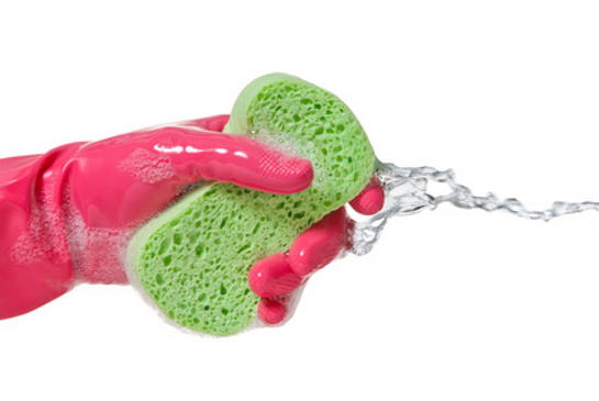 Ruka v ružovej rukavici držiaca zelenú hubku na riad
